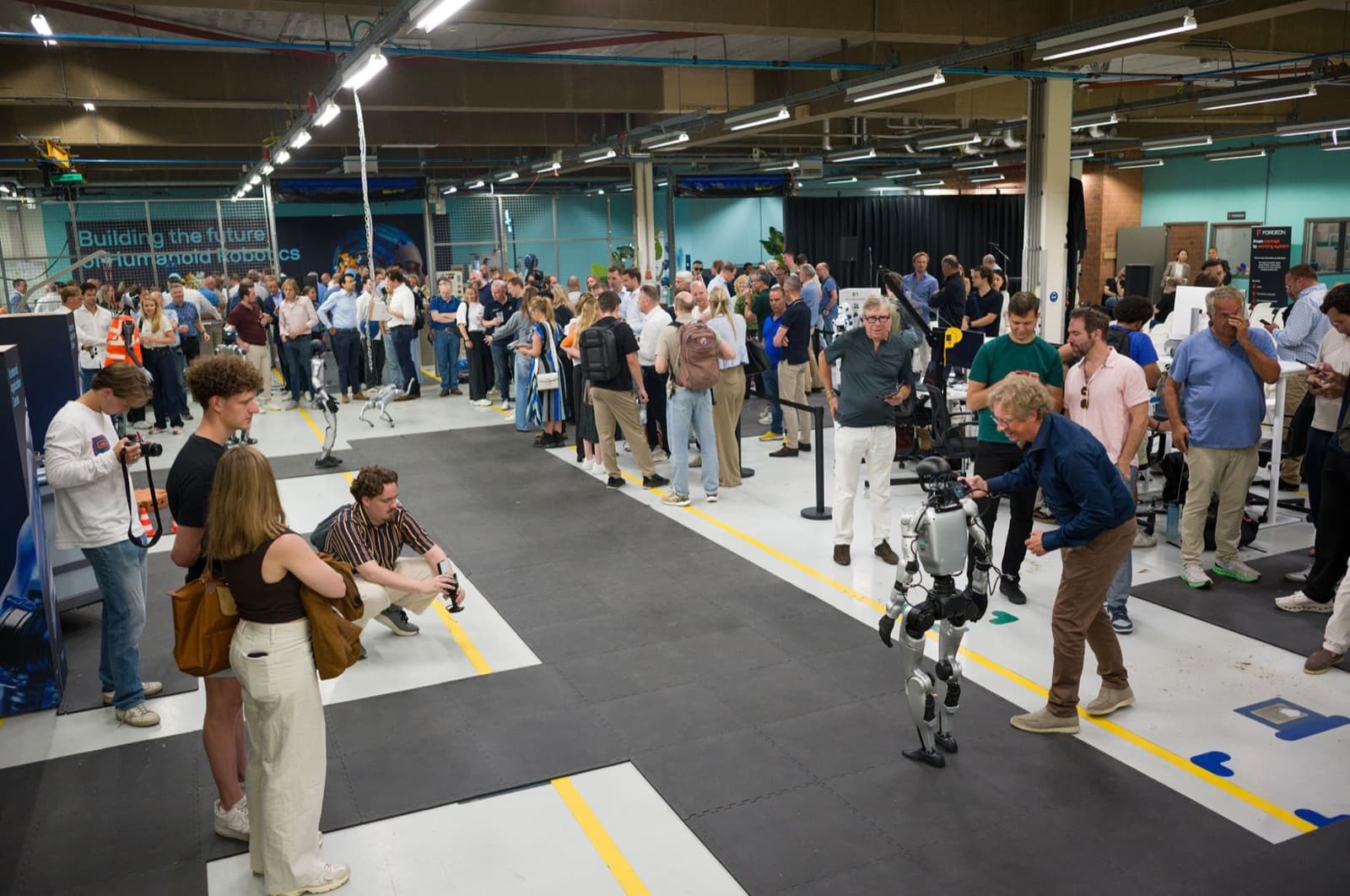Packed HAC opening: visitors around the humanoids on the shop floor, under the Building the future of Humanoid Robotics banner