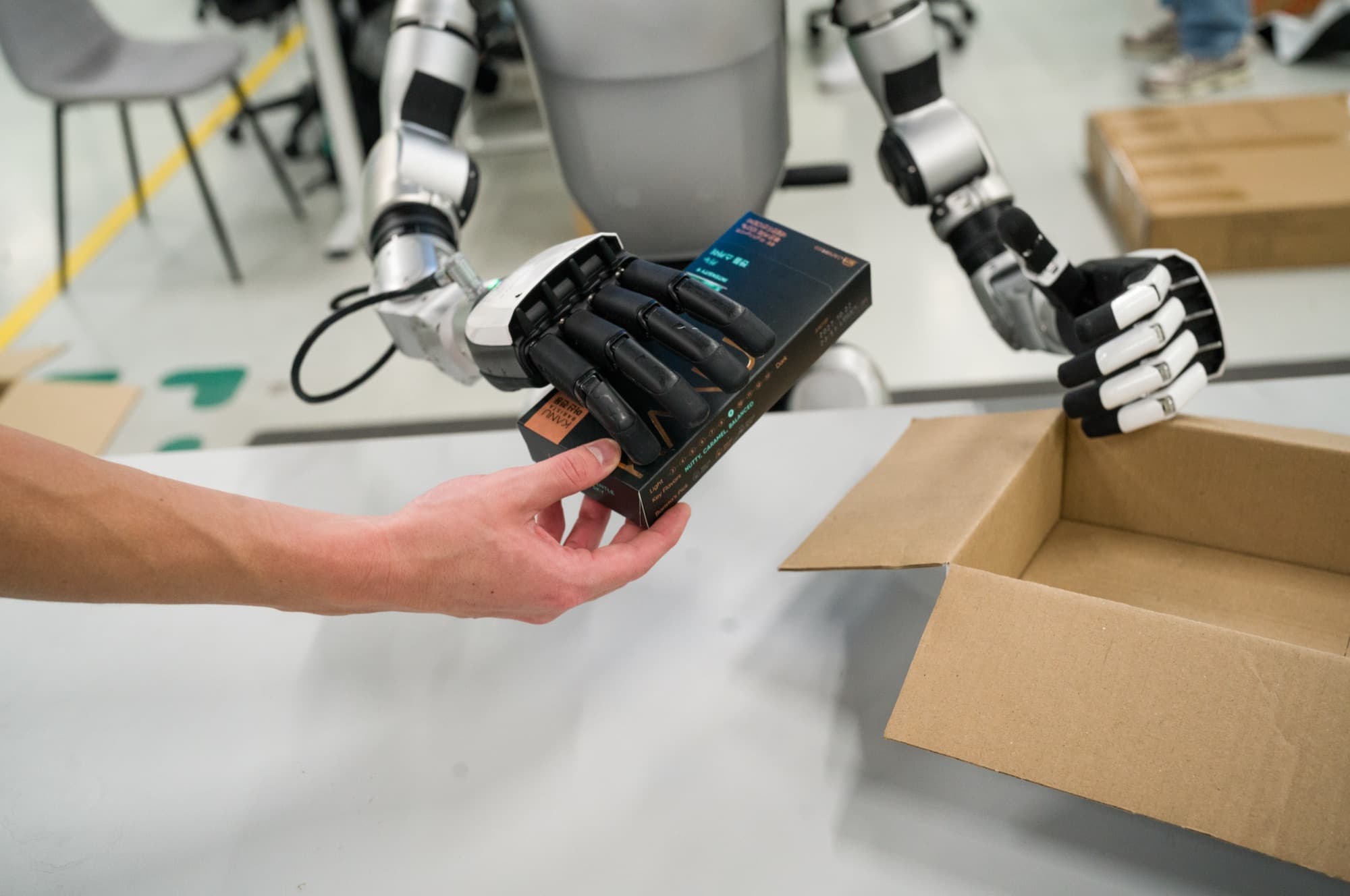Close-up van een mensenhand die een doosje aanreikt aan een robothand met vijf vingers