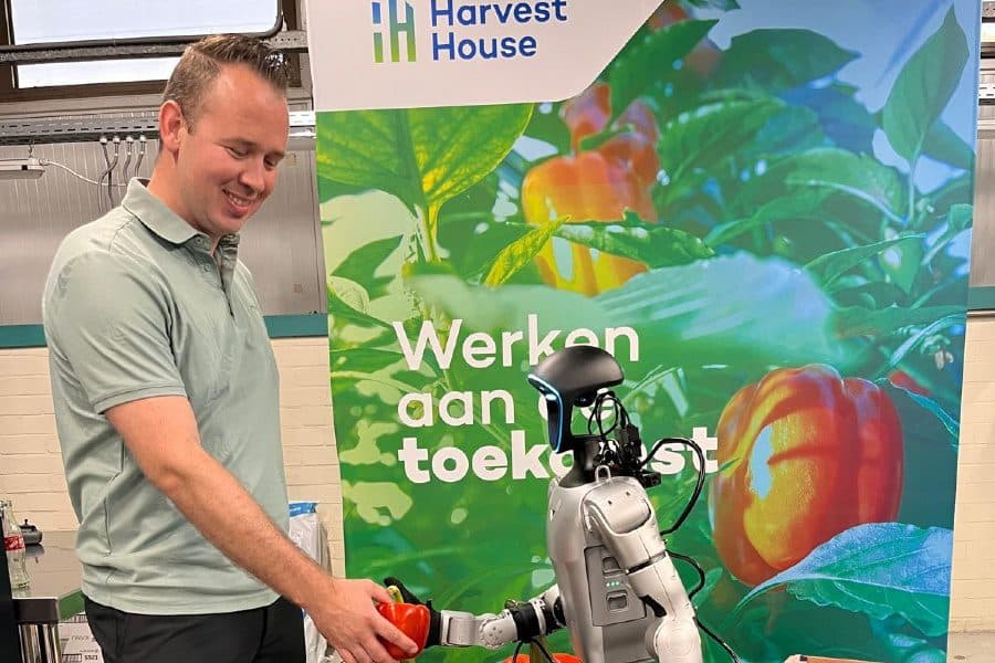Medewerker van Harvest House reikt een paprika aan een humanoid bij de Harvest House-stand